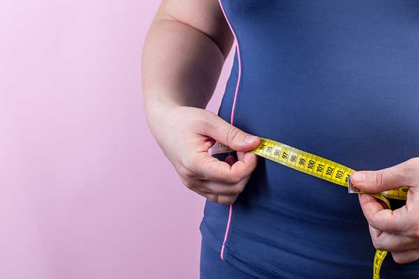 Upclose picture of a person measuring their midsection with a tape measure.