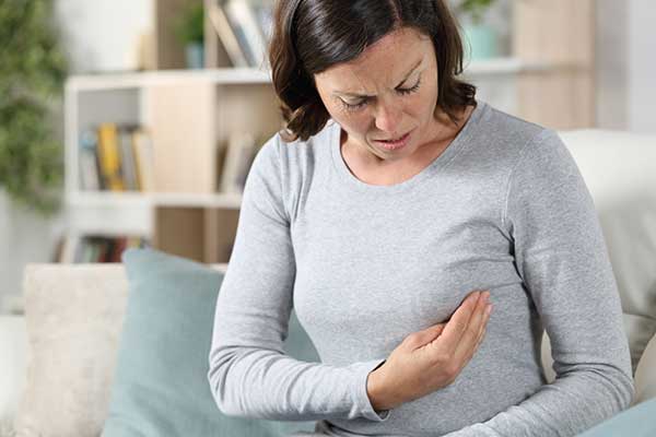 Woman looking down in discomfort while holding her left breast.