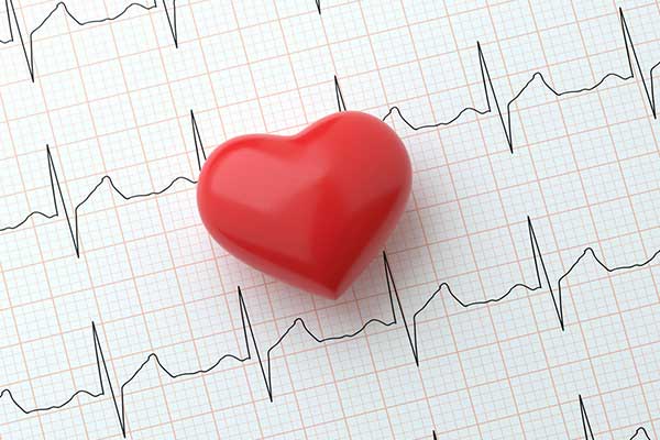 A red heart sits on a paper of ekg readings.