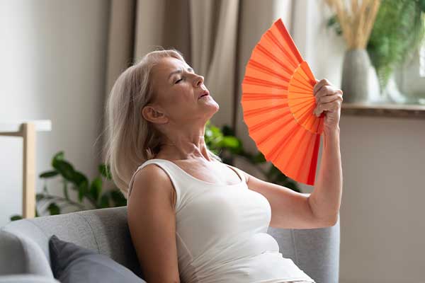 Woman sitting on a couch fanning herself with a fan.