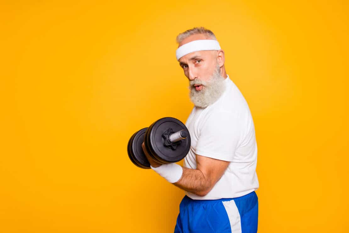 Cool playful strong grandpa with confident grimace exercising holding equipment up, lifts it with strength and power.